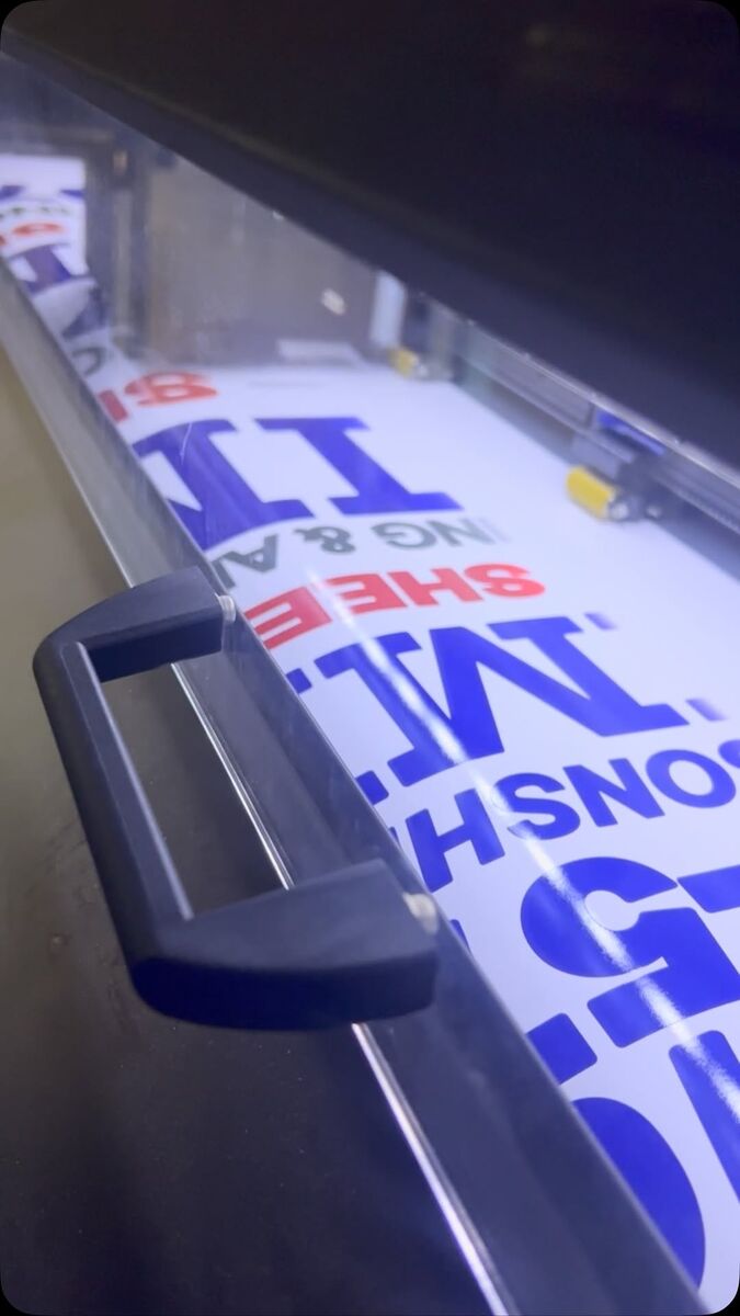 Freshly printed blue and white vinyl panel feeding out of a wide-format printer in the shop