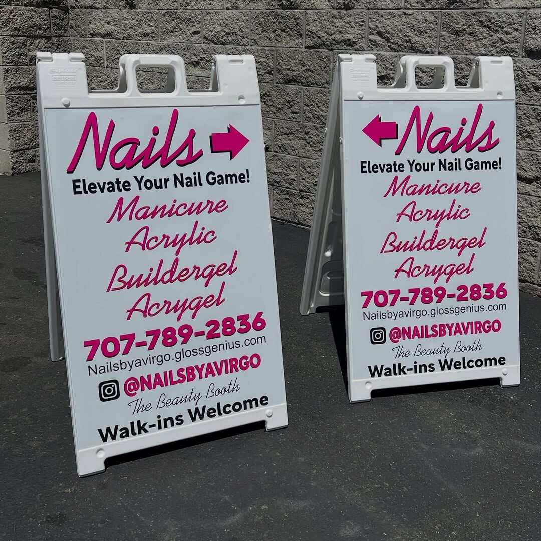 Two matching white A-frame signs for a nail salon, each with a pink directional arrow, a list of services and a phone number