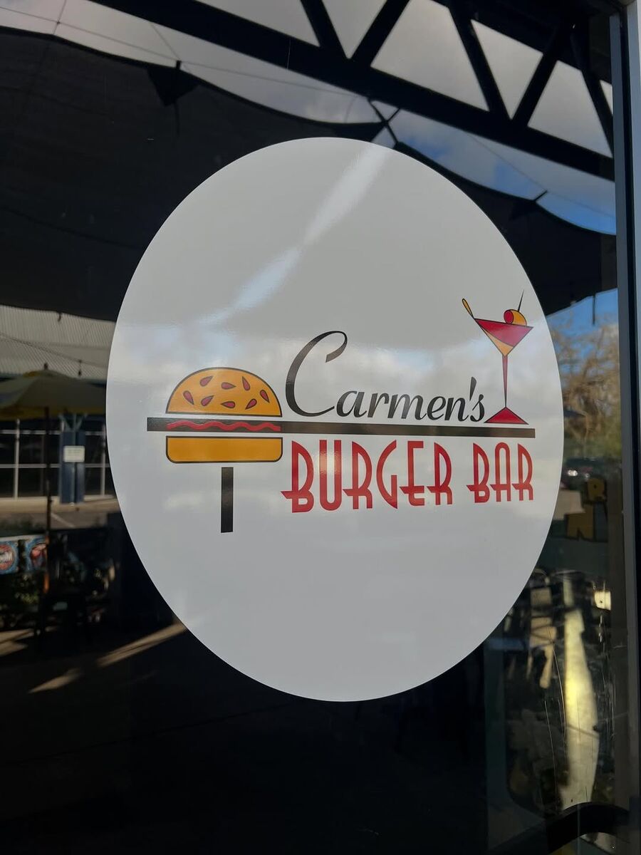 Circular Carmen's Burger Bar window graphic on glass, showing a burger and a cocktail above the wordmark