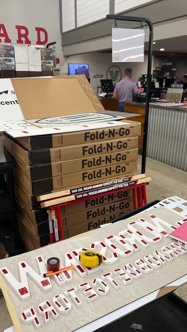 Red and white half-inch dimensional letters laid out in order on a workbench beside stacked cartons, ready to install