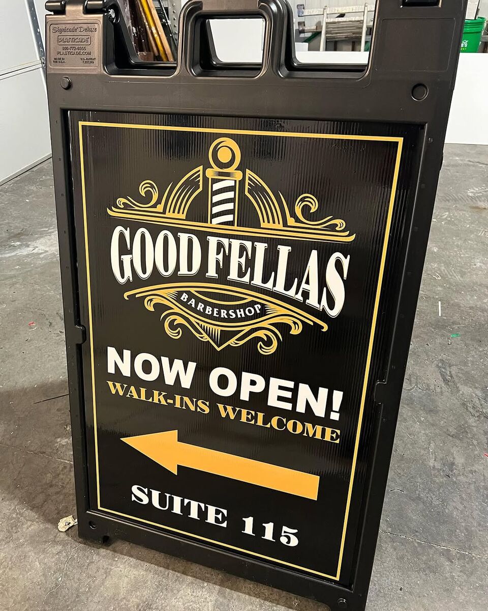 Black and gold Goodfellas Barbershop A-frame sign reading Now Open, Walk-ins Welcome, Suite 115, with an arrow