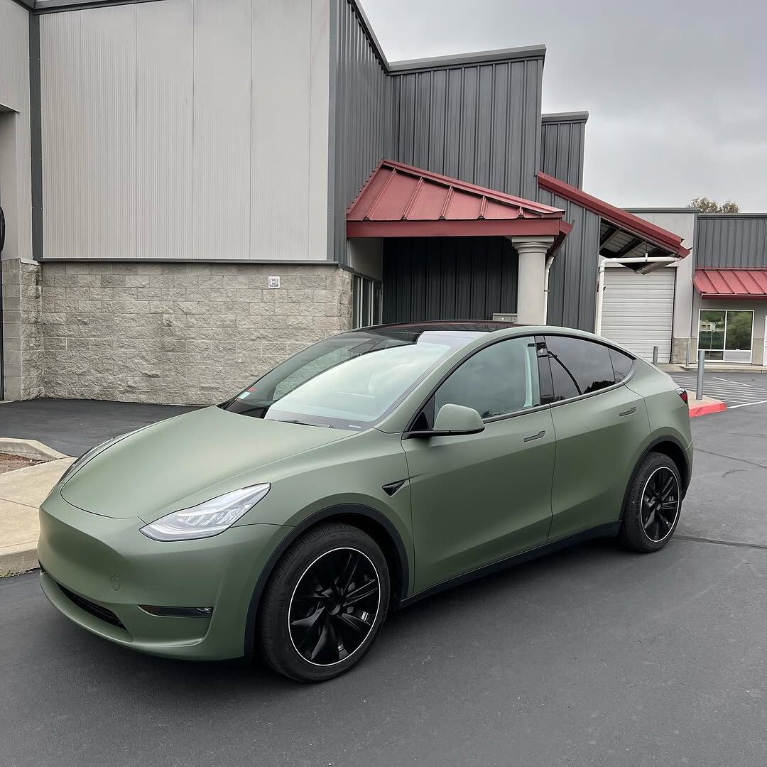 Tesla Model Y in a full matte military green colour change wrap, parked outside the shop