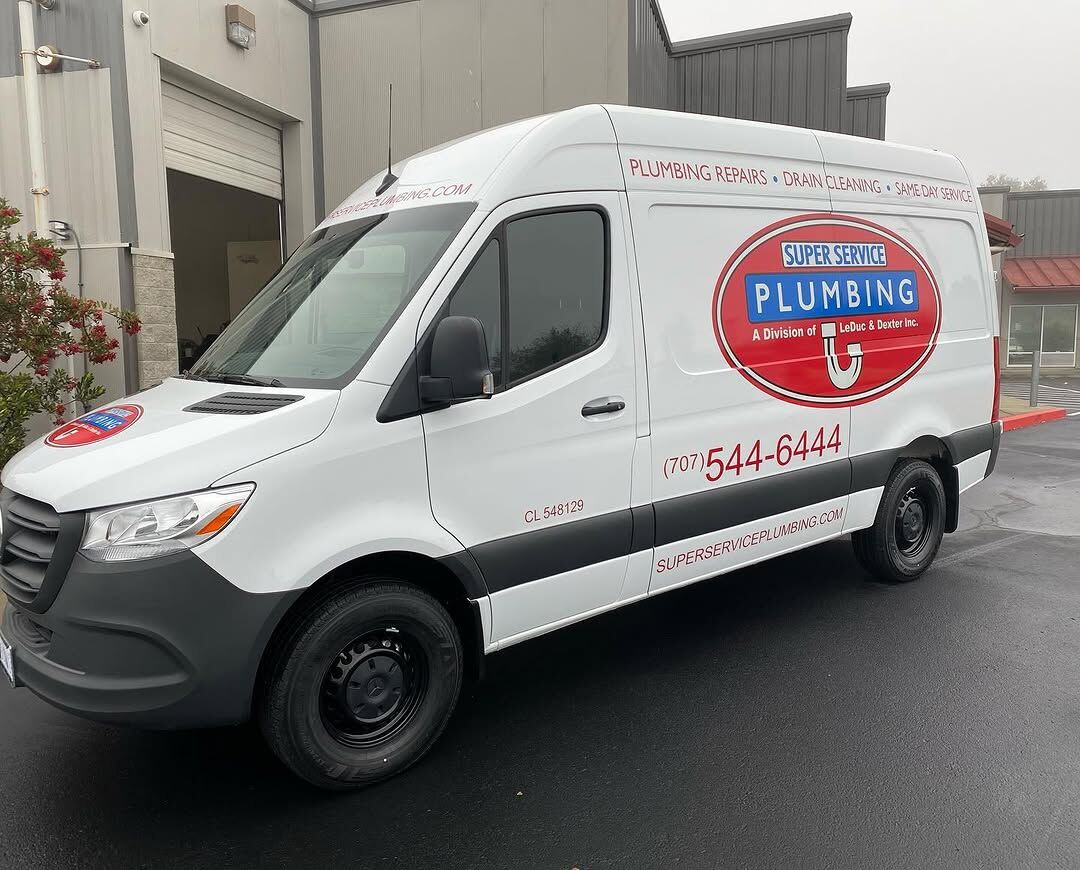 White Mercedes-Benz Sprinter van carrying red and blue Super Service Plumbing reflective graphics and a phone number