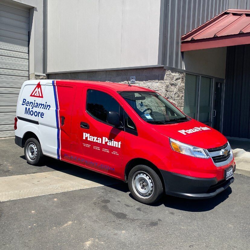 Red Plaza Paint delivery van with fresh graphics and a Benjamin Moore panel, parked outside the shop