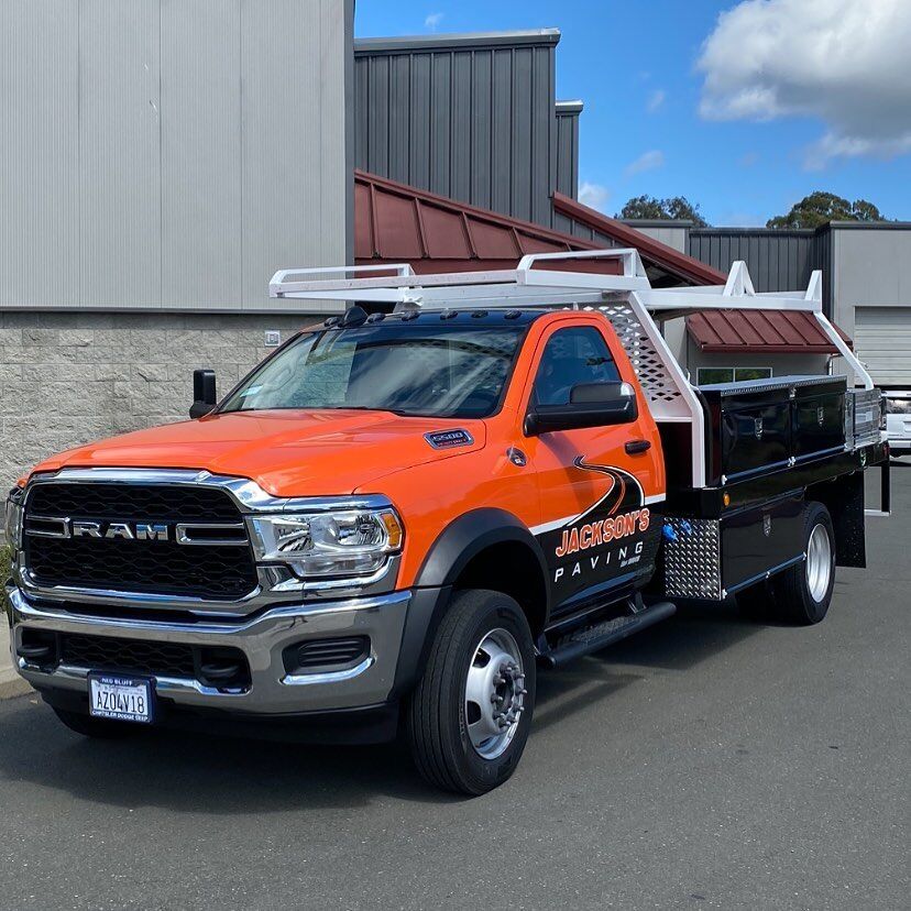 Orange and black Ram flatbed tow truck in a full wrap, parked outside the shop