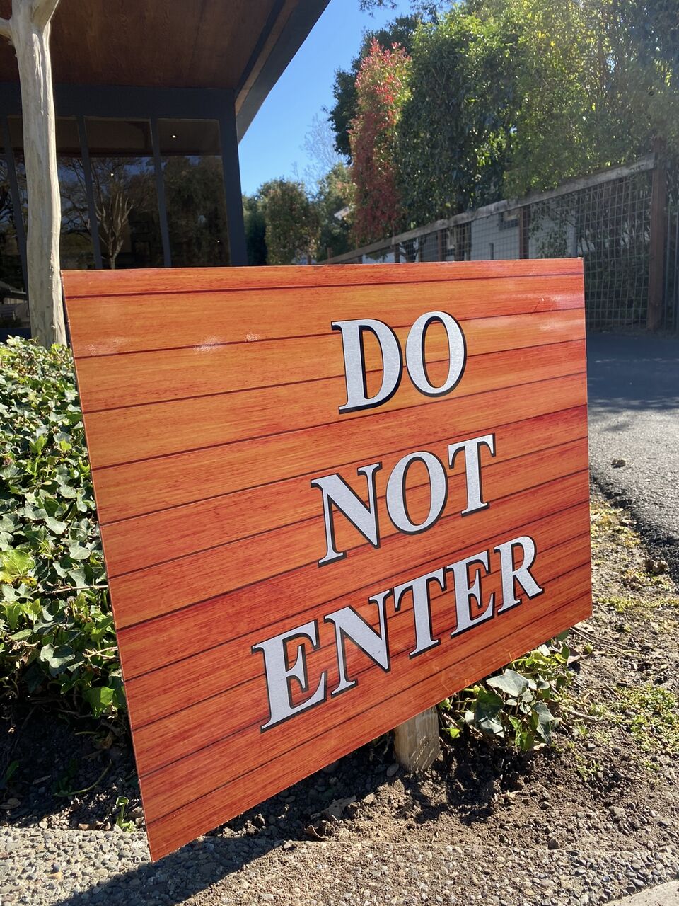 Wood-grain post-mounted sign reading Do Not Enter in raised silver letters, set in planting beside the driveway