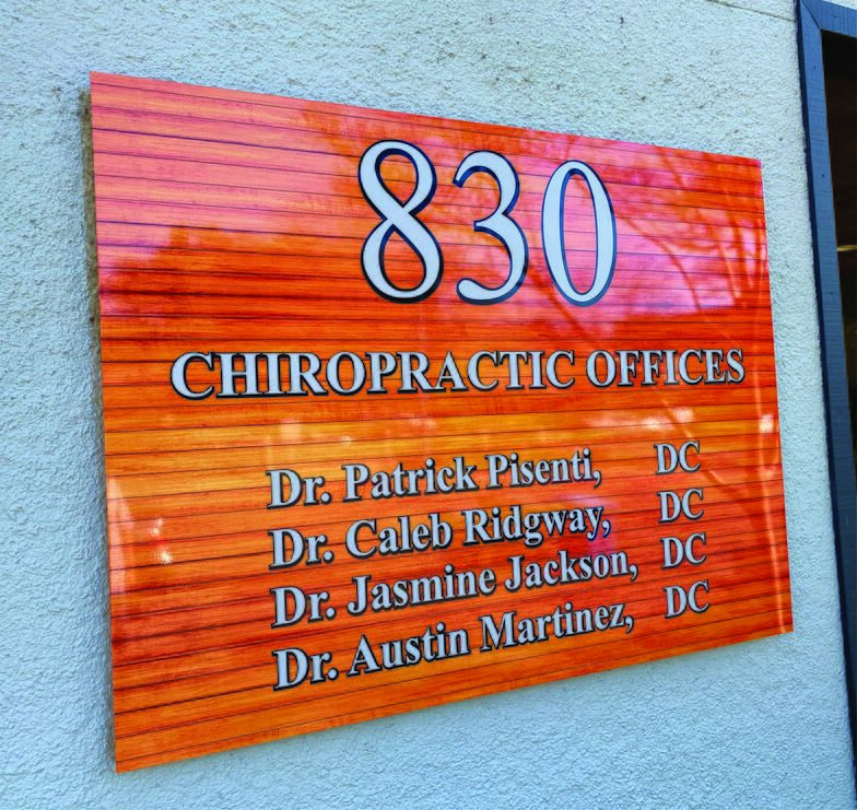 Dimensional sign on a wood-grain panel reading 830 Chiropractic Offices with four doctors' names