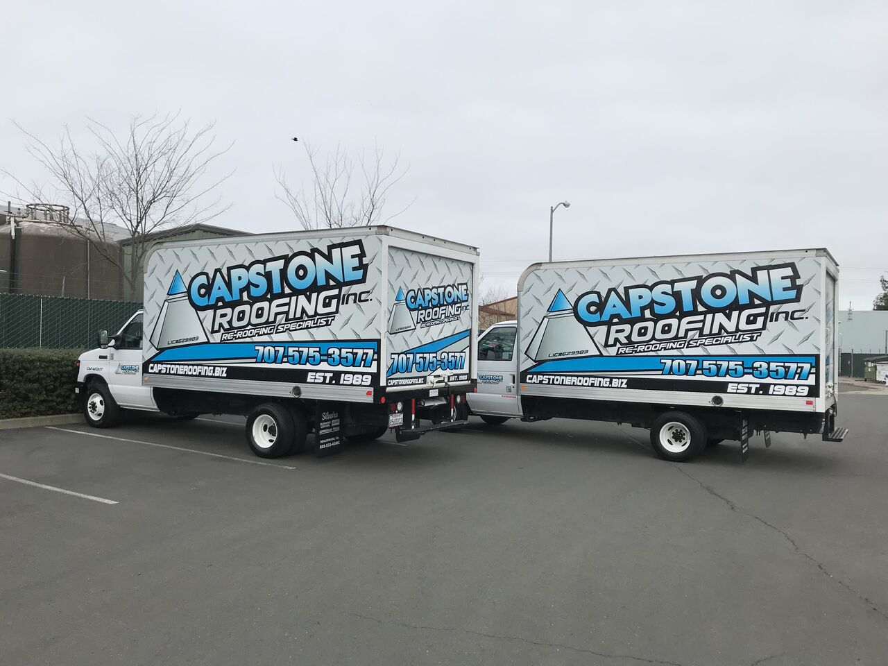 Two matching Capstone Roofing box trucks parked side by side with identical blue and white graphics