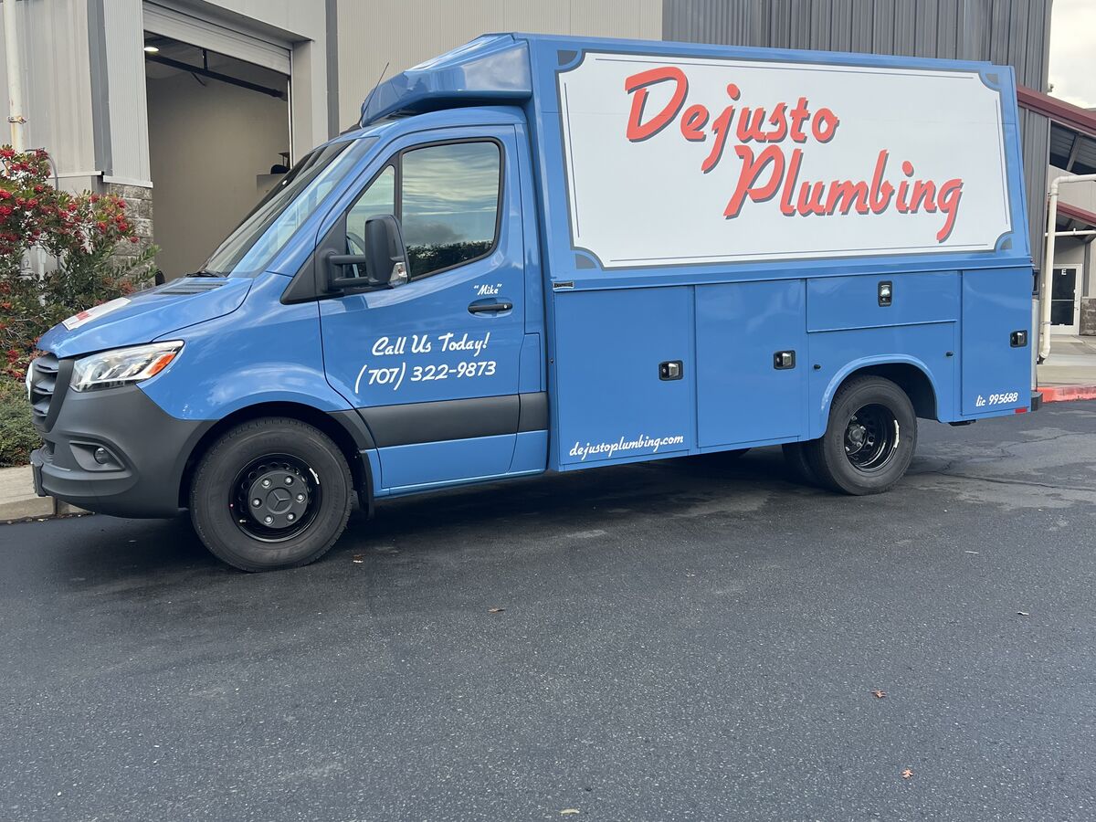 Blue Mercedes-Benz Sprinter service body van with a white panel carrying the Dejusto Plumbing script logo and a call-us line on the cab door