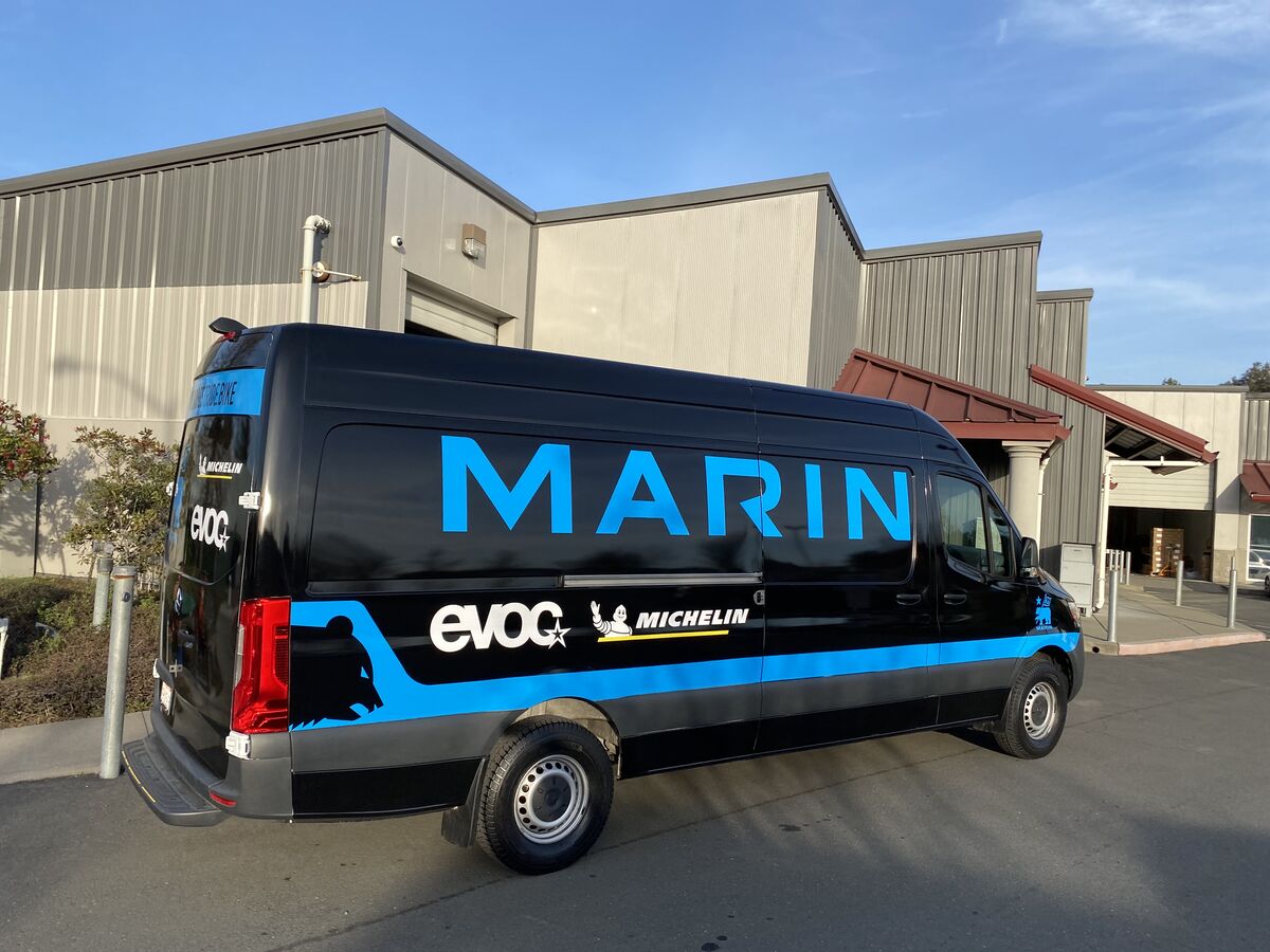 Black Mercedes-Benz Sprinter van wrapped for Marin with the name in large blue letters along the flank and sponsor marks on the lower band