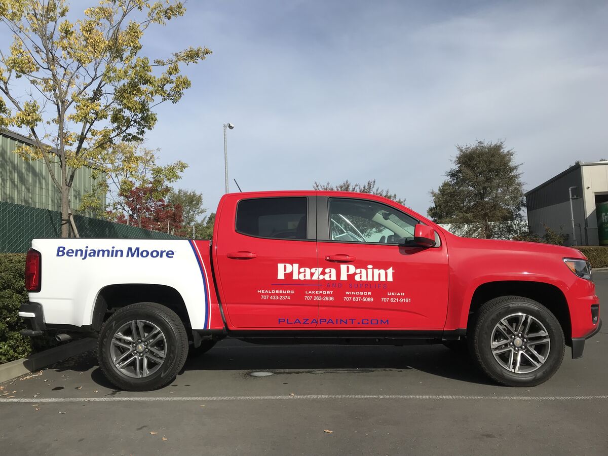 Red and white Chevrolet Colorado pickup carrying Plaza Paint graphics on the doors, four branch towns listed beneath, and a Benjamin Moore panel on the bed side