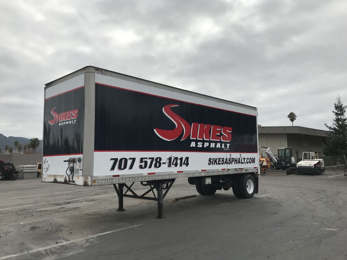 Box trailer wrapped in black with the Sikes Asphalt mark in red across the side and the phone number and website along the lower white band