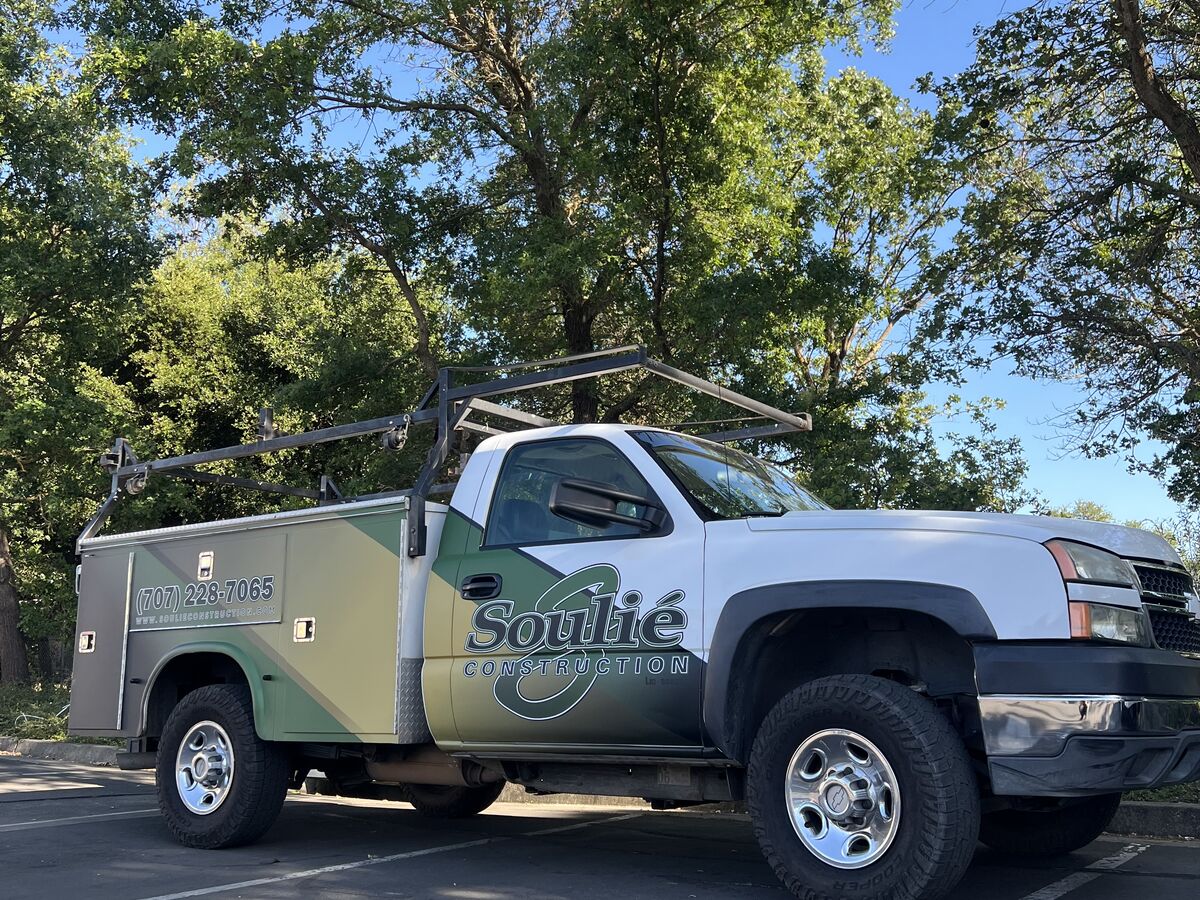 Souli&eacute; Construction utility pickup with a ladder rack, wearing the same green and gold diagonal livery as the box vans